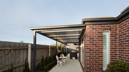 Modern brick home with covered outdoor patio, gable roof carport with polycarbonate panels, and concrete driveway in landscaped backyard