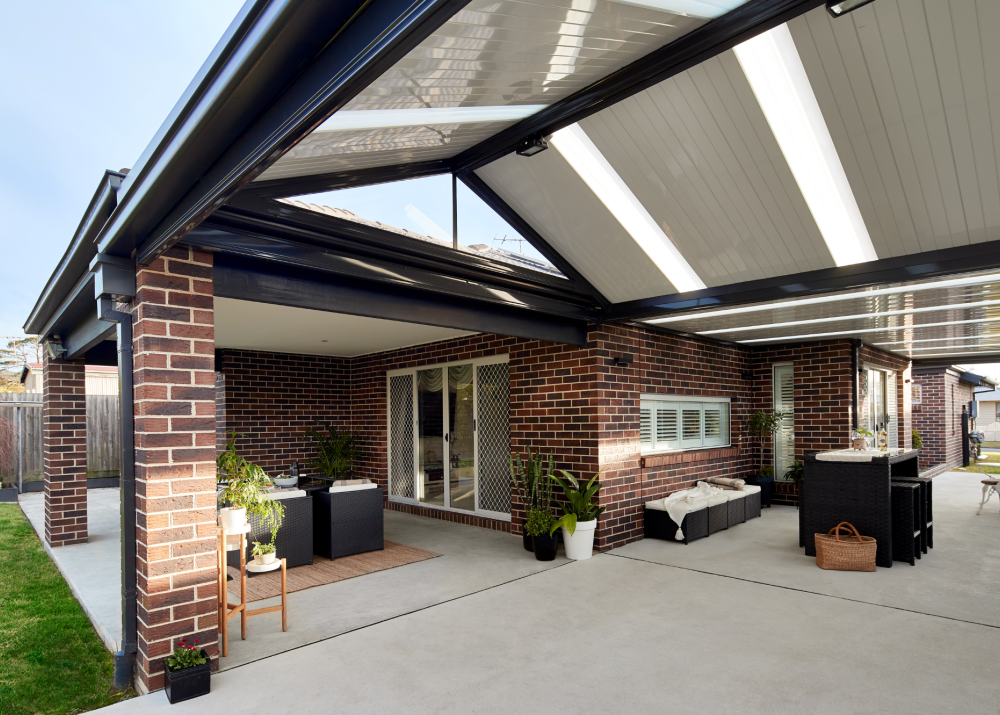 Attached steel pergola with a gable roof and light-reflective panels over a brick patio area.